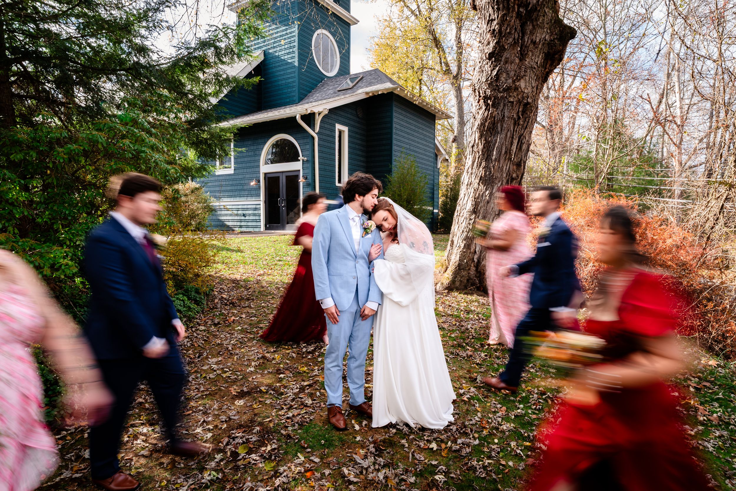 A joyful wedding celebration in motion outside a charming blue chapel in autumn.