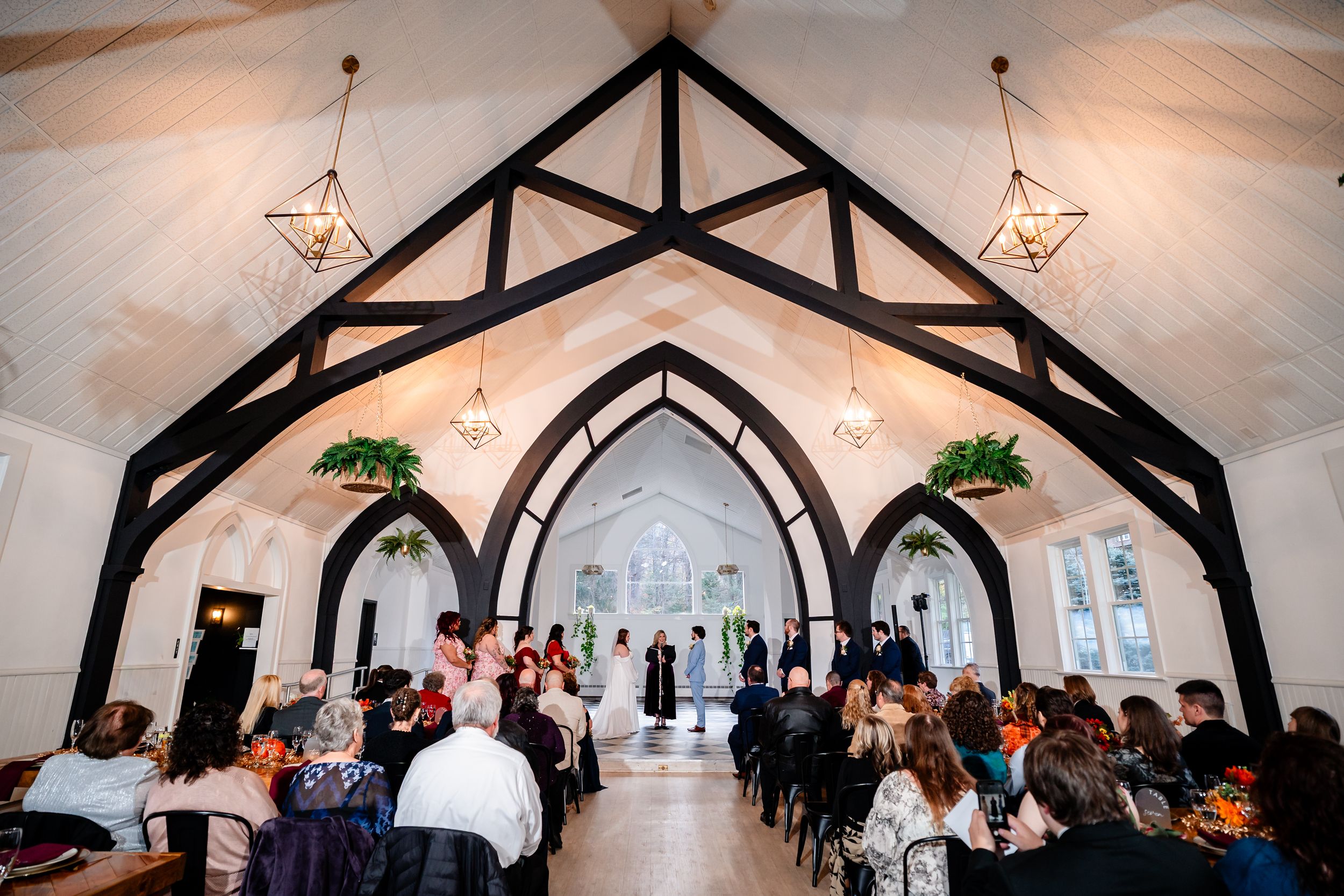 A wedding ceremony takes place inside a rustic wooden chapel with exposed beams and white walls.