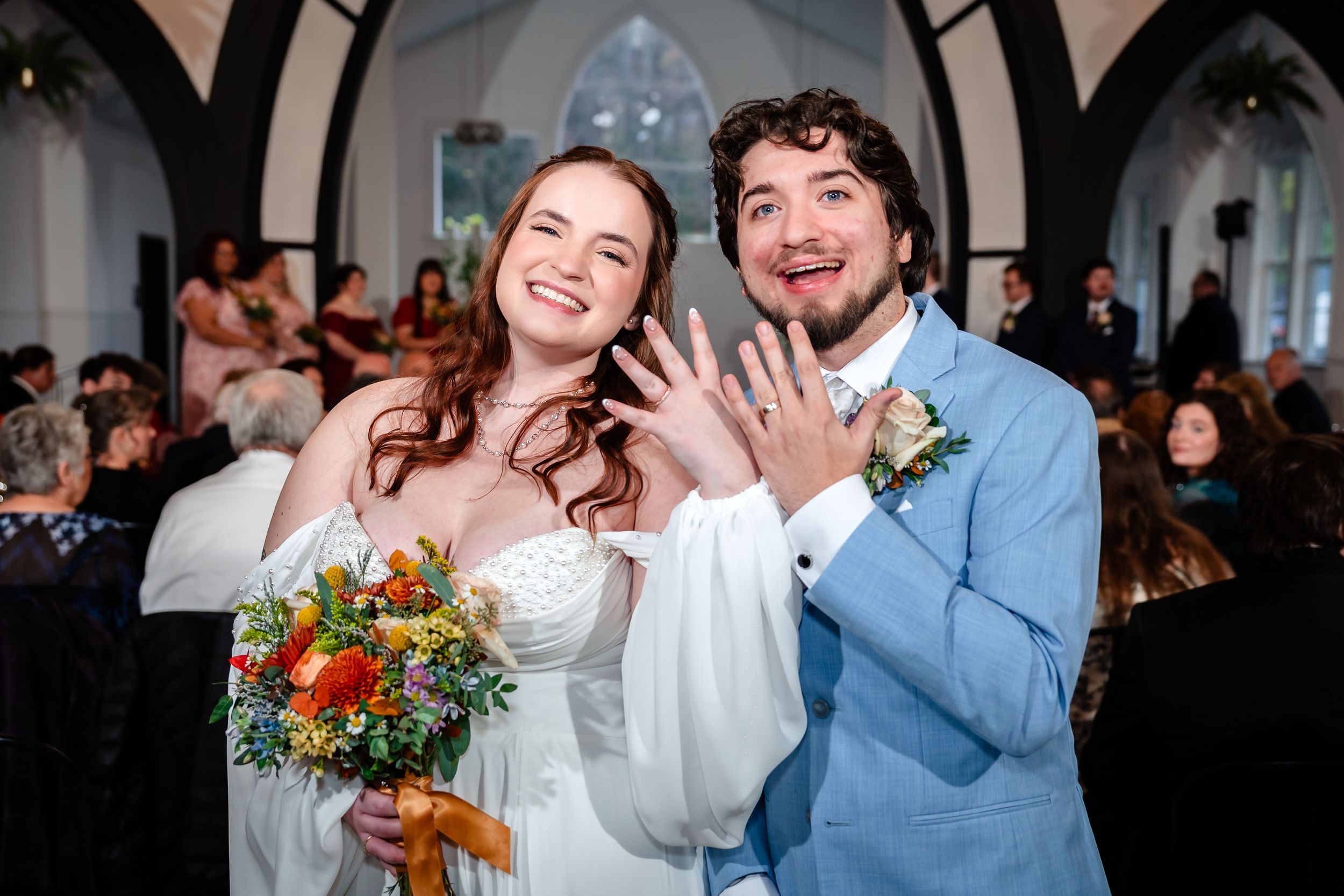 A couple shares a joyful moment during their wedding celebration with guests and floral decorations in the background.