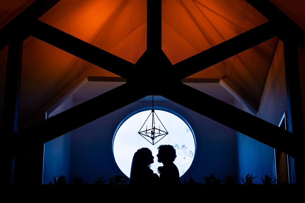 A silhouetted couple shares a romantic moment against a bright full moon backdrop through a window frame.