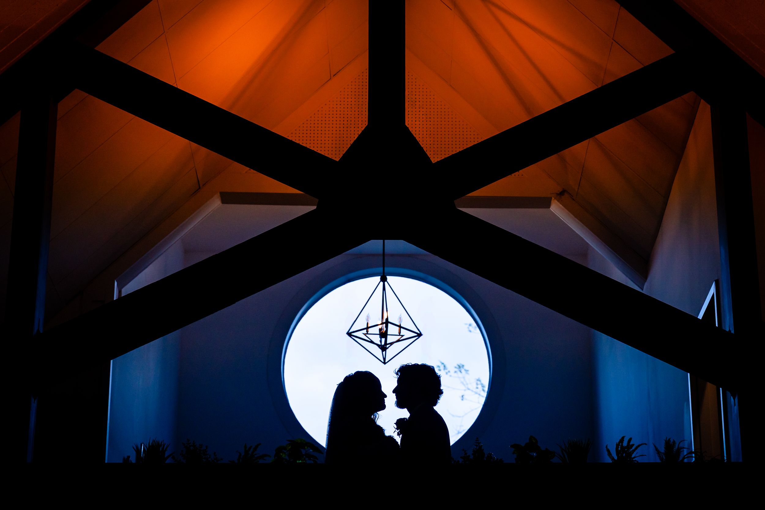 A silhouetted couple shares a romantic moment against a bright full moon backdrop through a window frame.