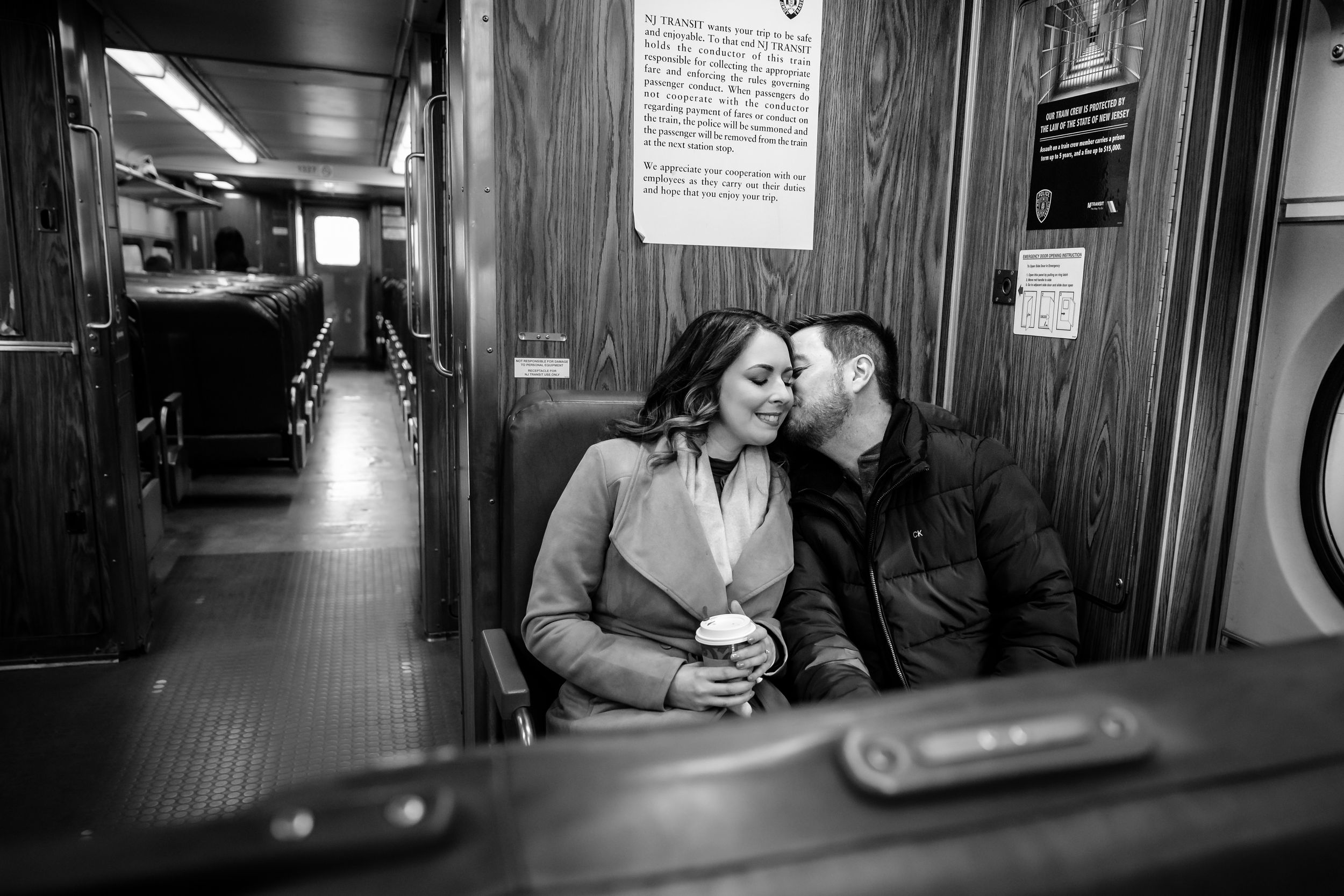 Black and white photograph of a subway car interior with passengers seated along the walls during a commute.
