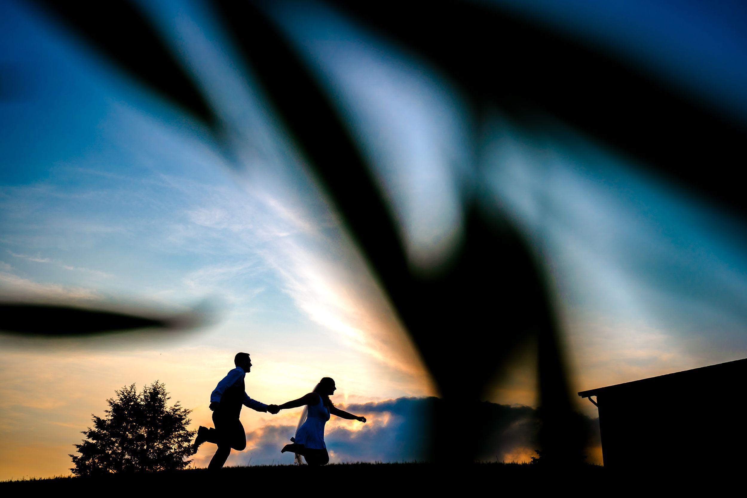 Silhouettes against a dramatic blue and orange sunset sky create artistic wedding photography.