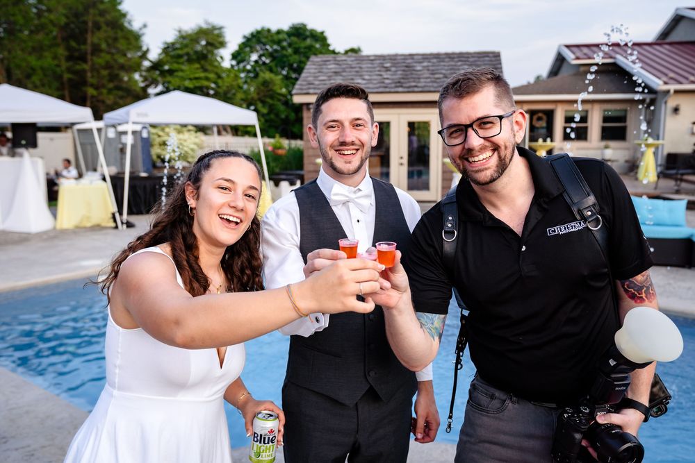A wedding celebration by a pool with people toasting drinks outdoors on a summer day.