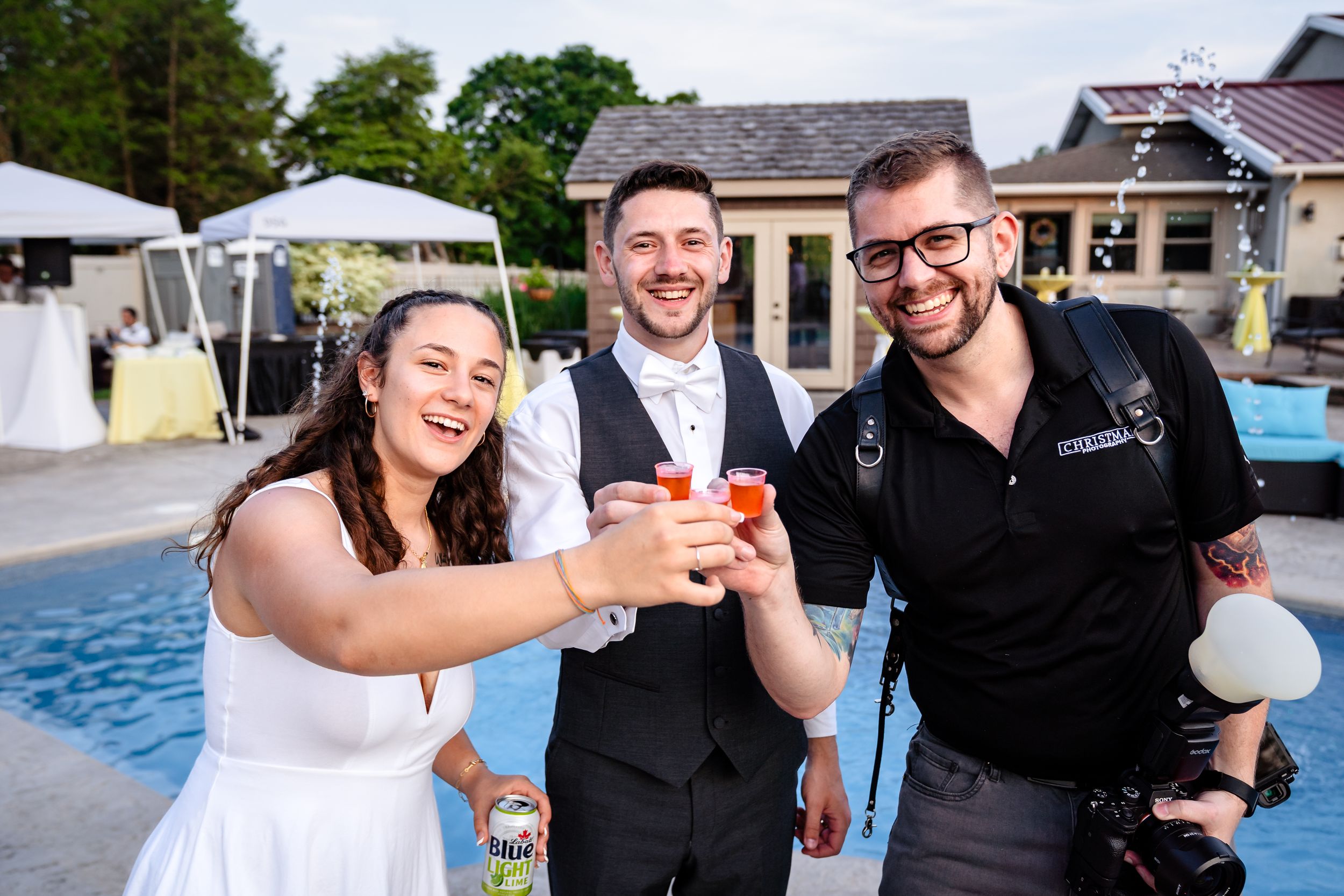 A wedding celebration by a pool with people toasting drinks outdoors on a summer day.