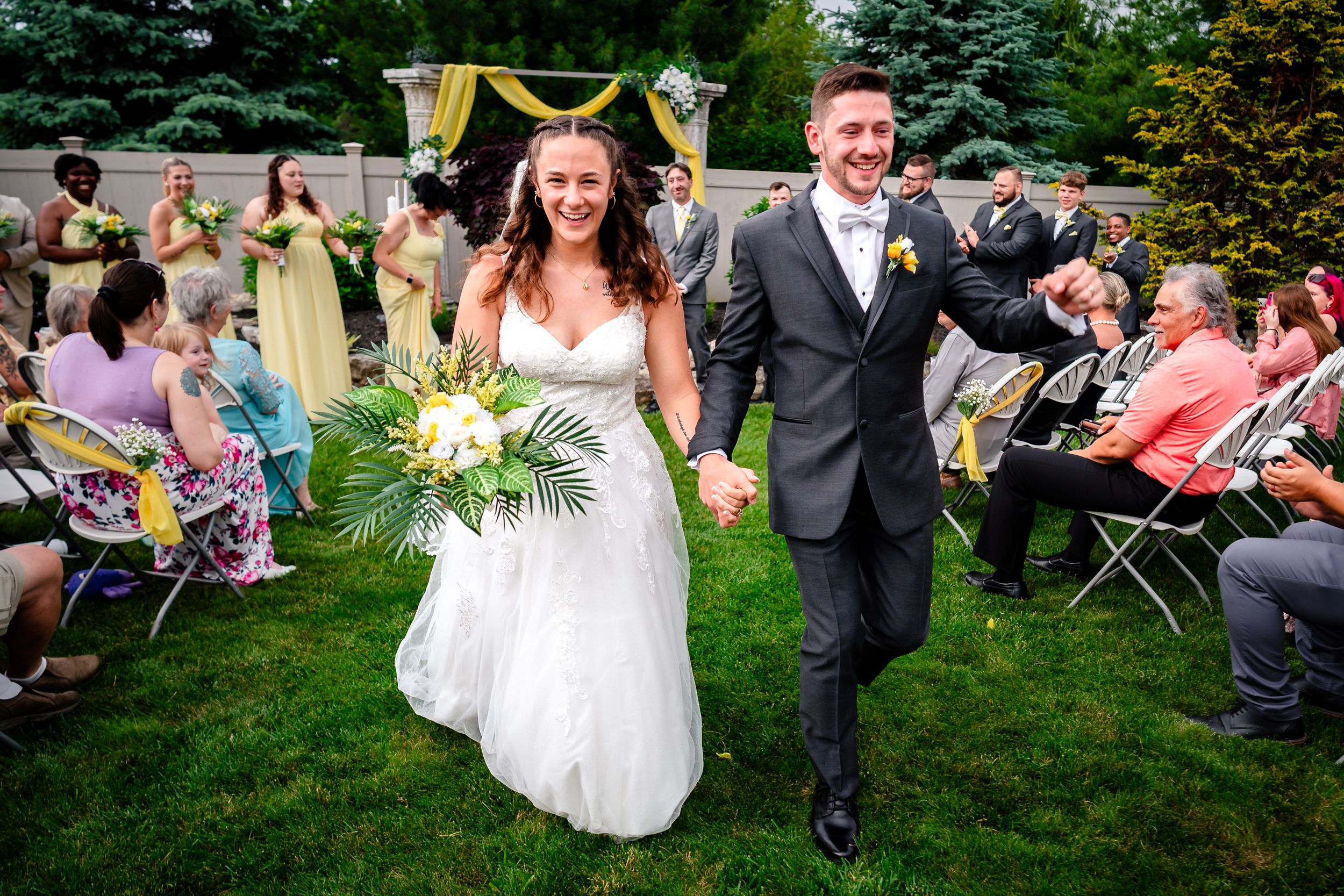 Wedding party dances together in a lush green garden setting during an outdoor celebration.