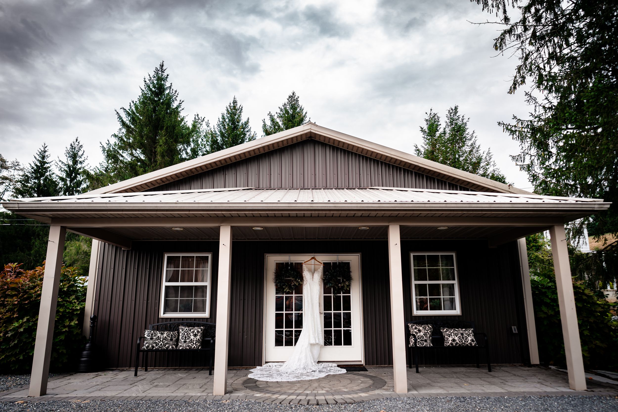 A modern rustic wedding venue exterior with dark siding, white double doors, and a covered front porch.
