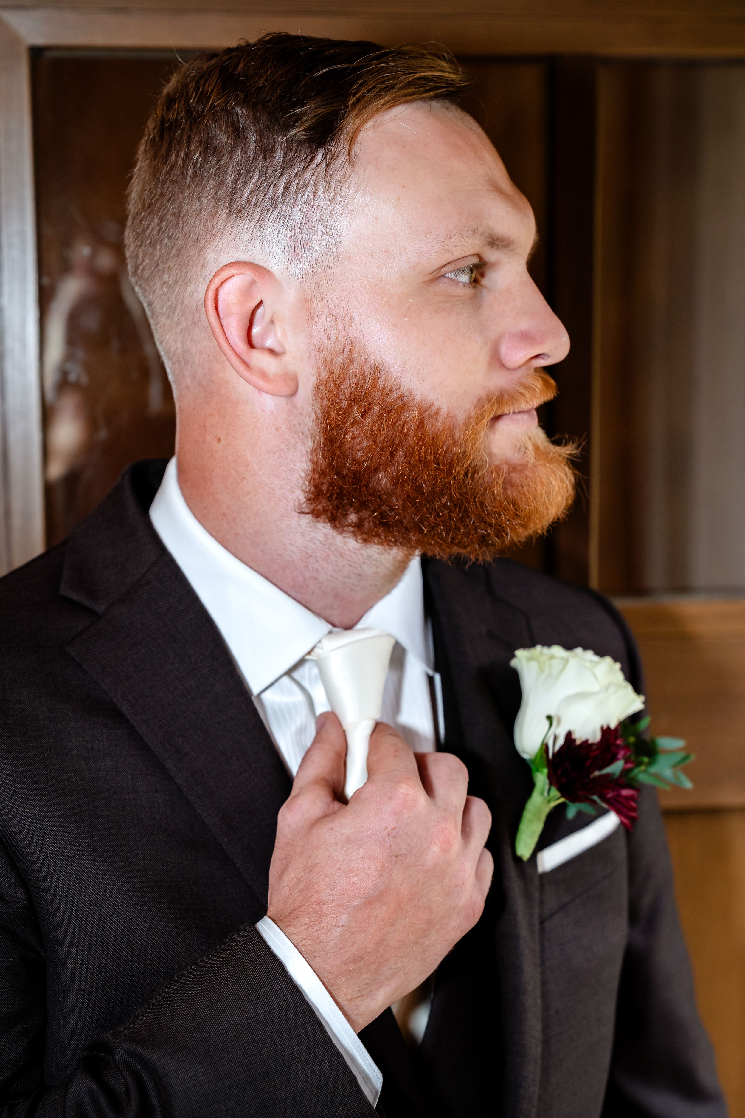 A groom in a black suit adjusts his white tie while wearing a white rose boutonniere in a series of photos.