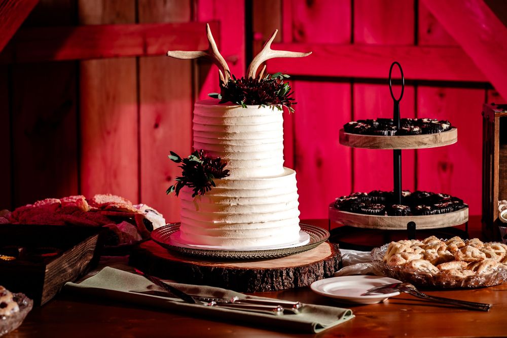 Wedding reception dessert table with white tiered cake and assorted cookies displayed against a dramatic red backdrop.