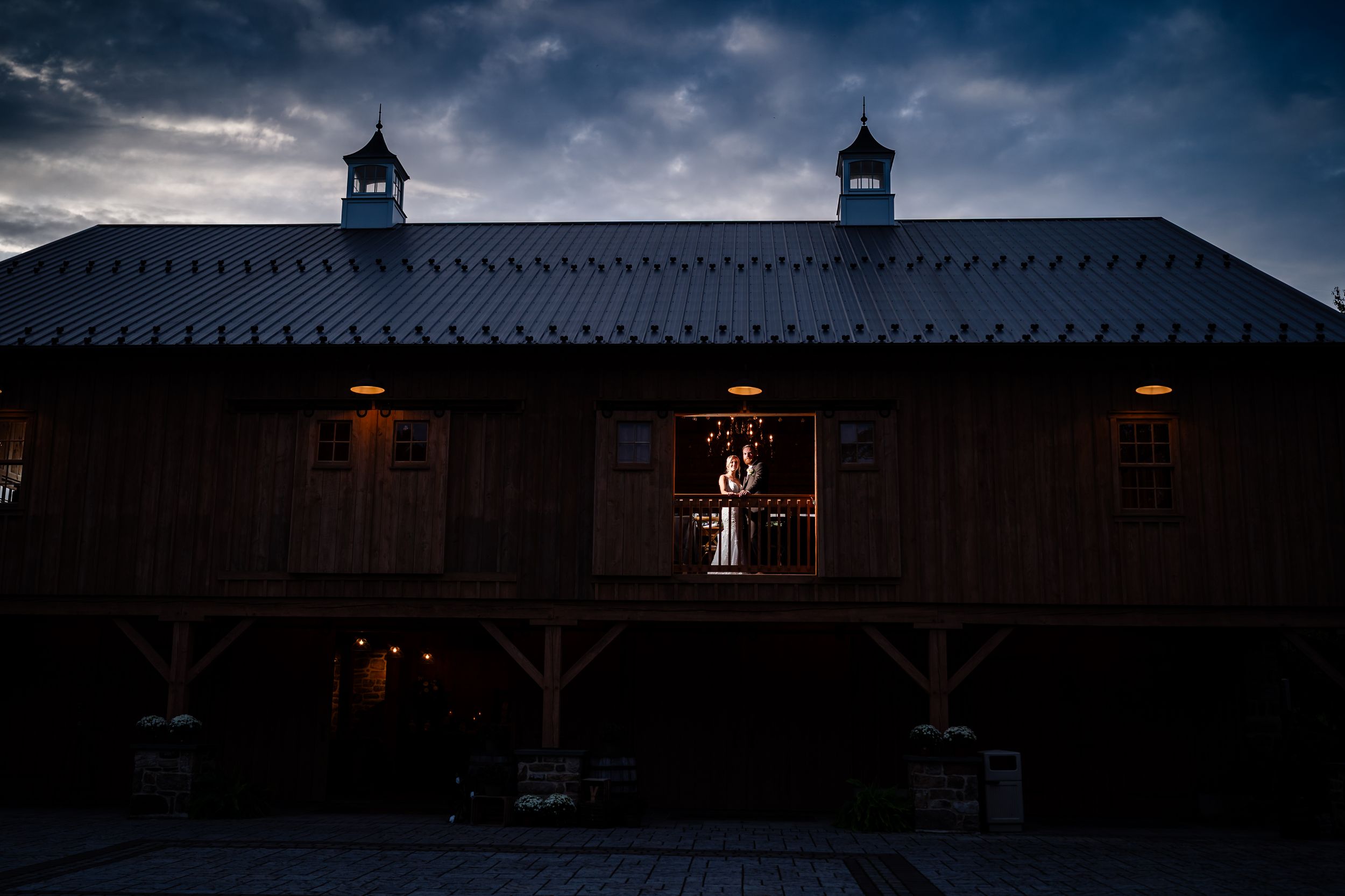 Dark moody wedding venue exterior with dramatic cloudy sky and silhouetted architectural details.