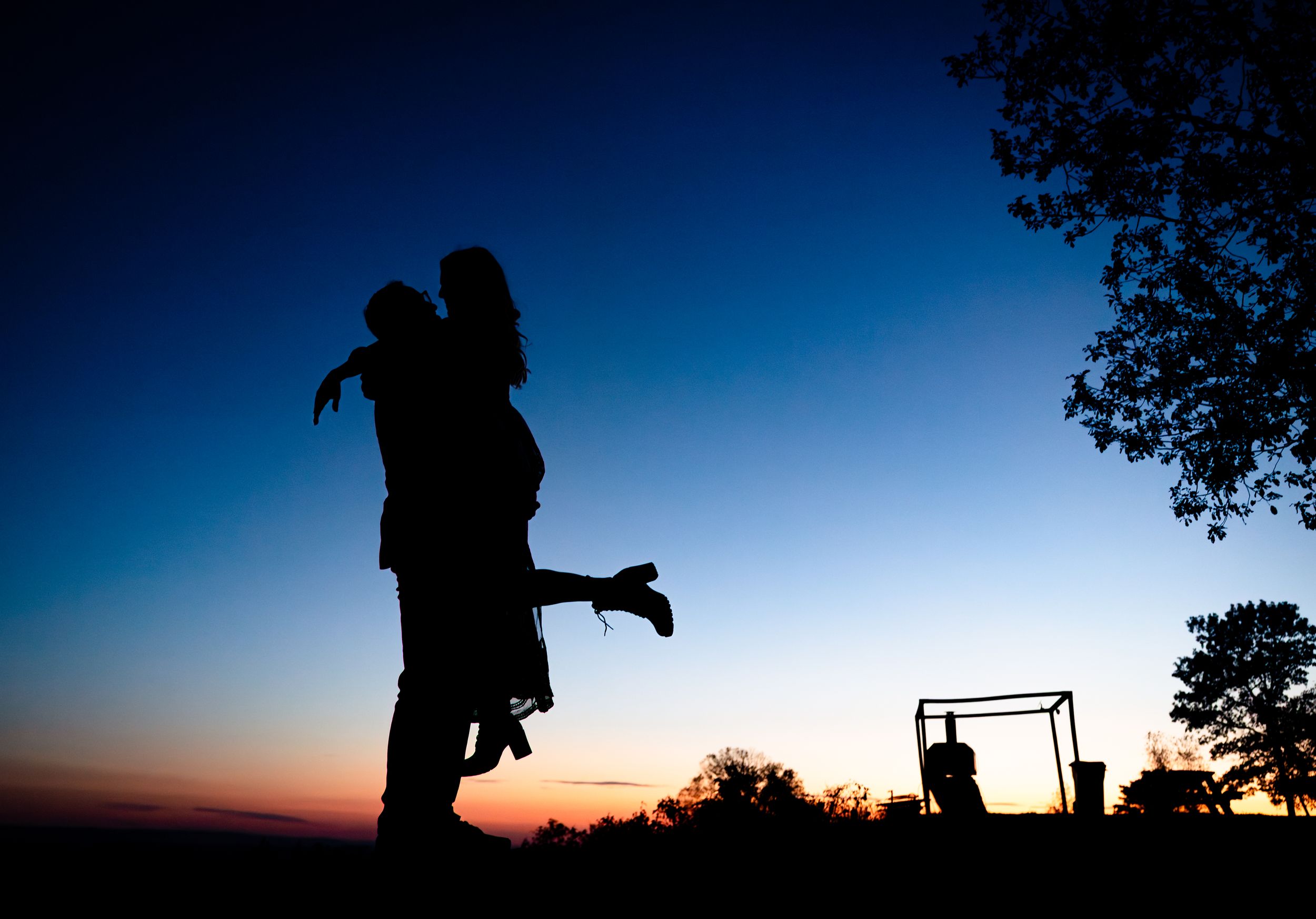 A series of silhouetted figures hiking against a vibrant sunset sky with trees and mountains in the background.