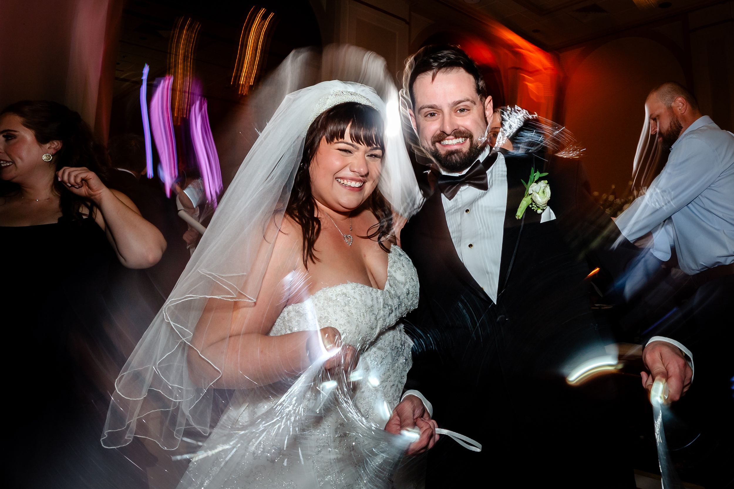 Wedding guests dance and celebrate on a dimly lit dance floor during an evening reception celebration.
