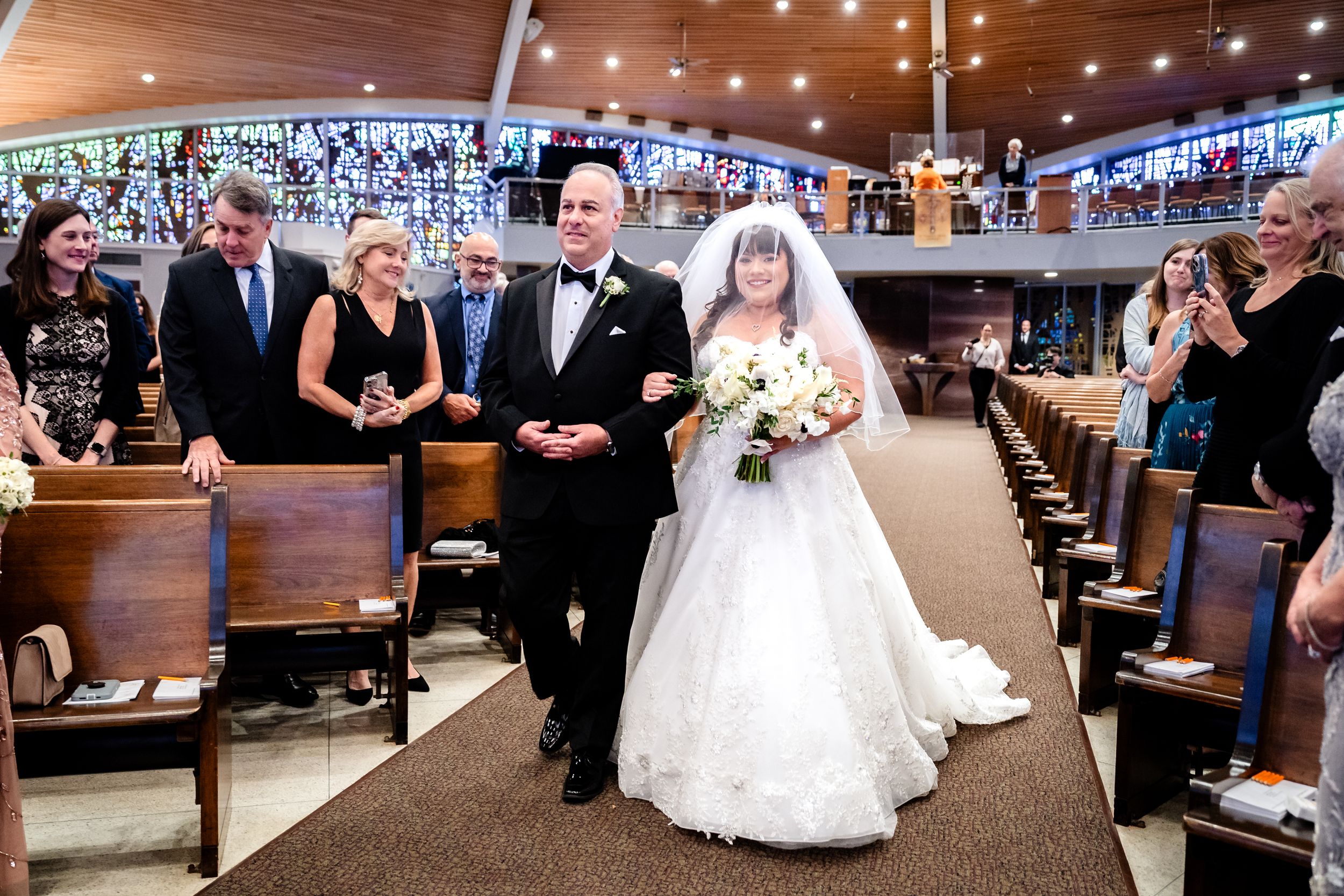 A traditional church wedding processional with attendees watching from wooden pews.