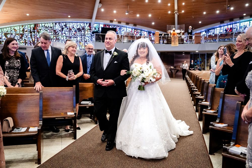 A traditional church wedding processional with attendees watching from wooden pews.