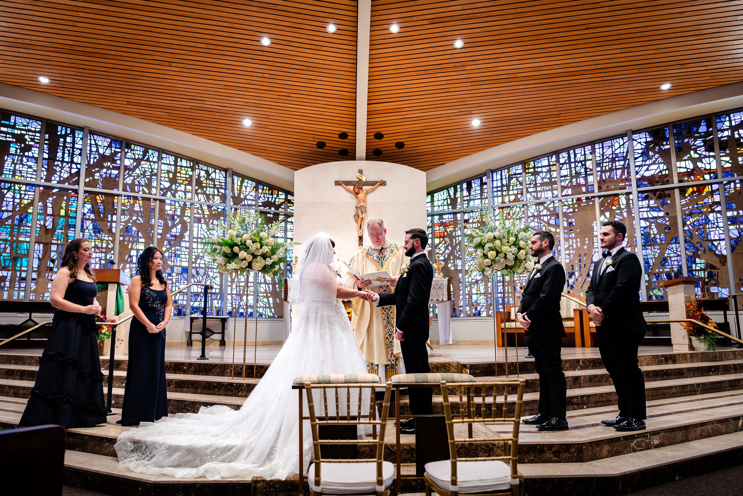 Wedding ceremony in a church with stained glass windows and wooden ceiling beams.