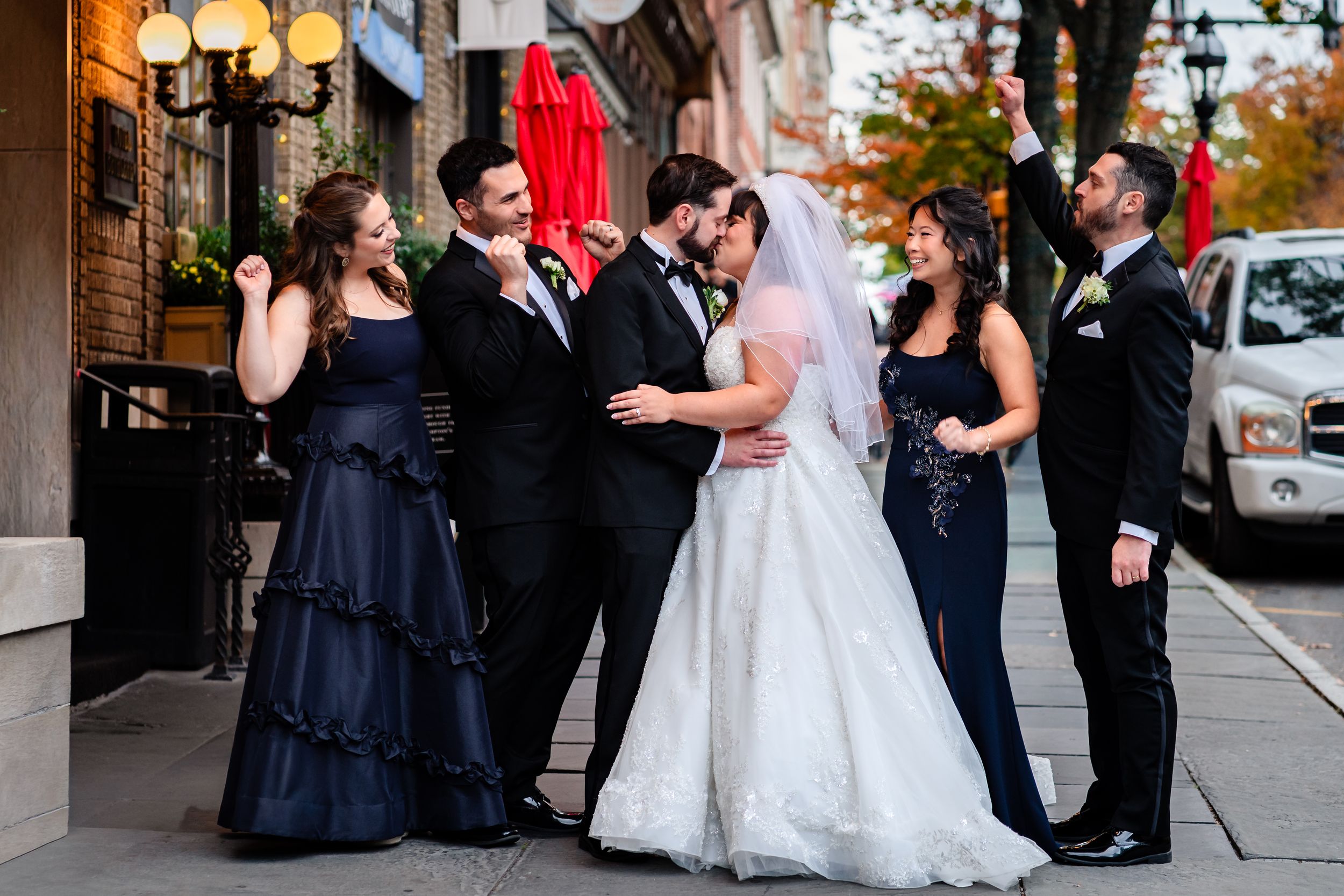 Wedding party in navy blue and white poses together on outdoor brick sidewalk.