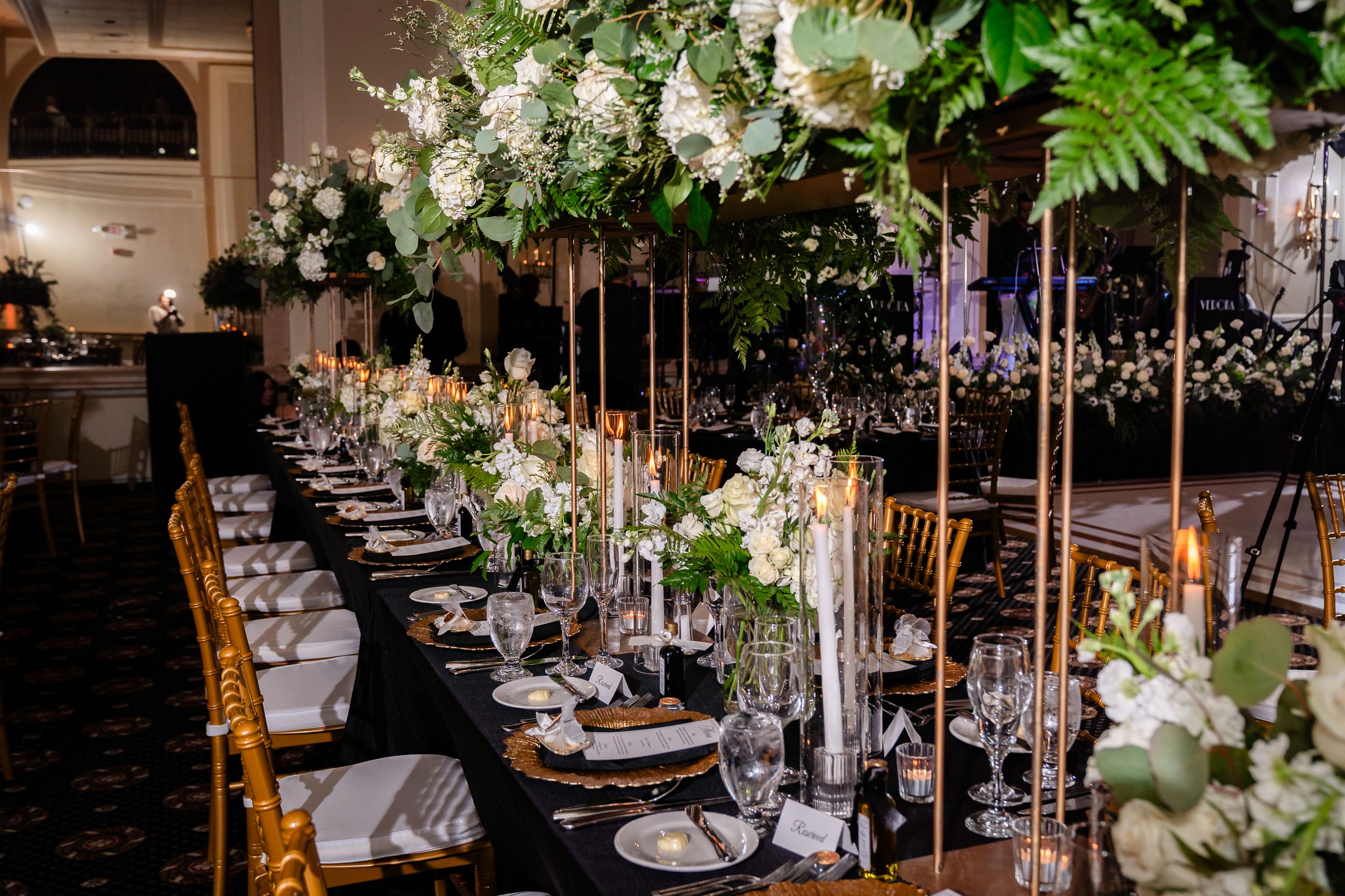 An elegant indoor wedding reception with hanging floral arrangements and crystal chandeliers decorating the dining tables.