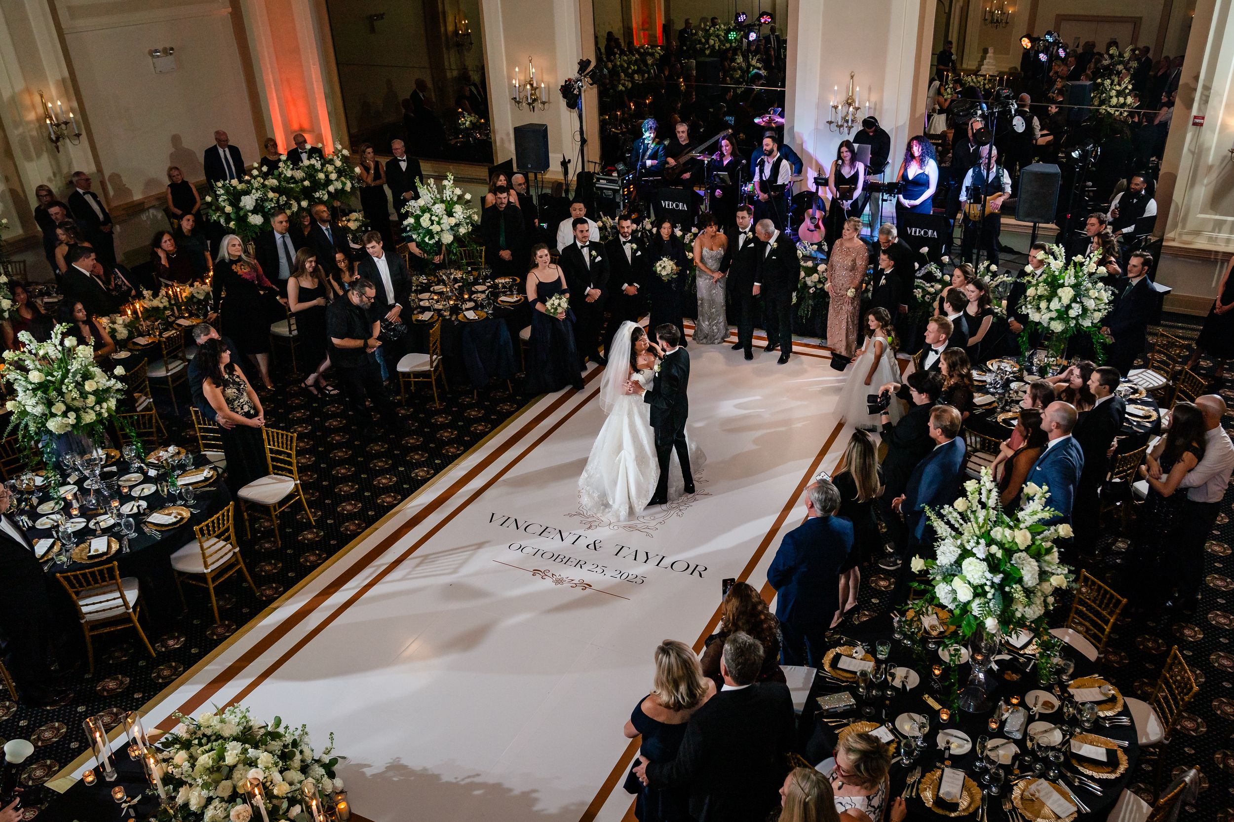 Large wedding reception hall with elegant lighting and floral centerpieces on round tables.