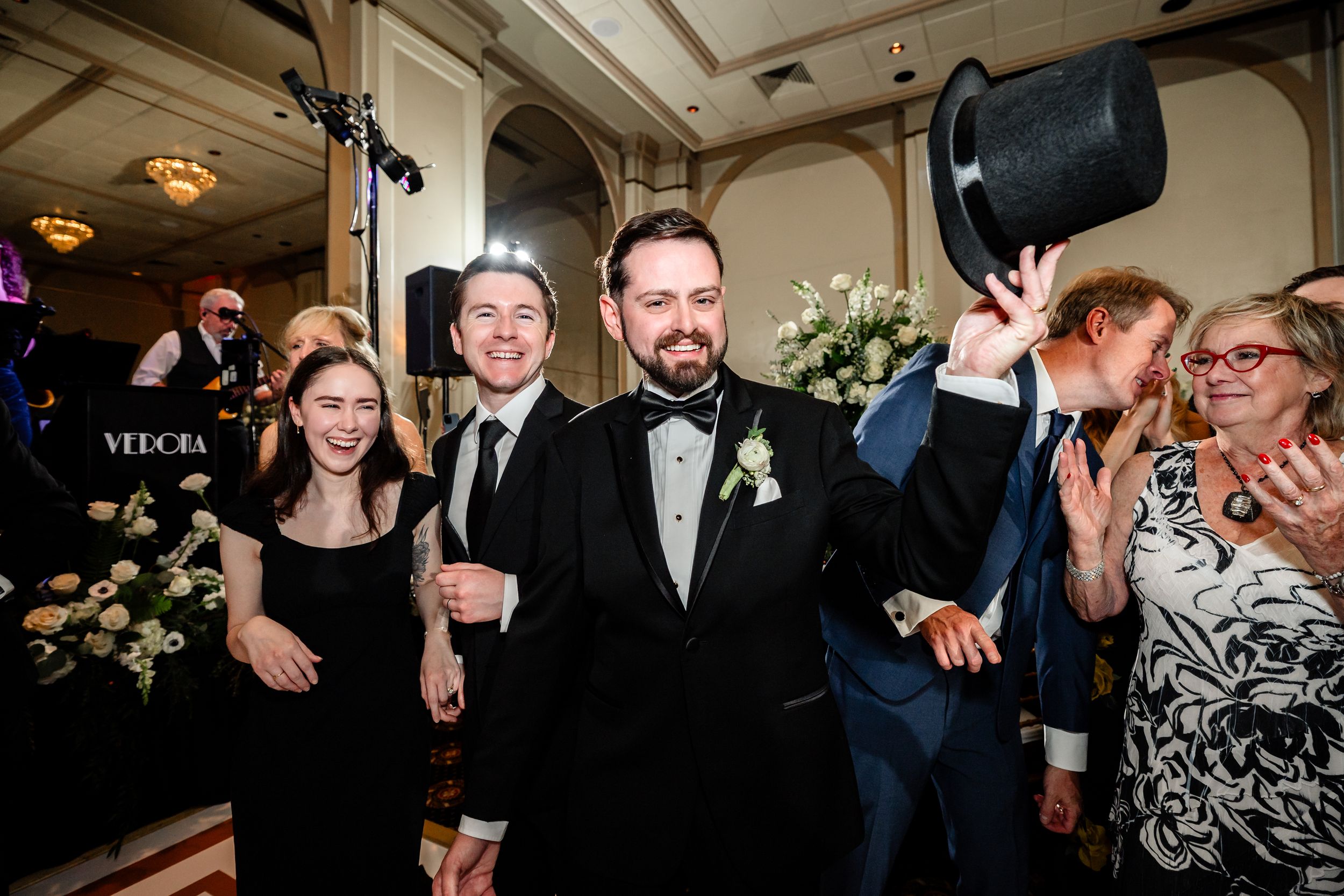 Wedding guests dancing and celebrating on dimly lit dance floor at reception.
