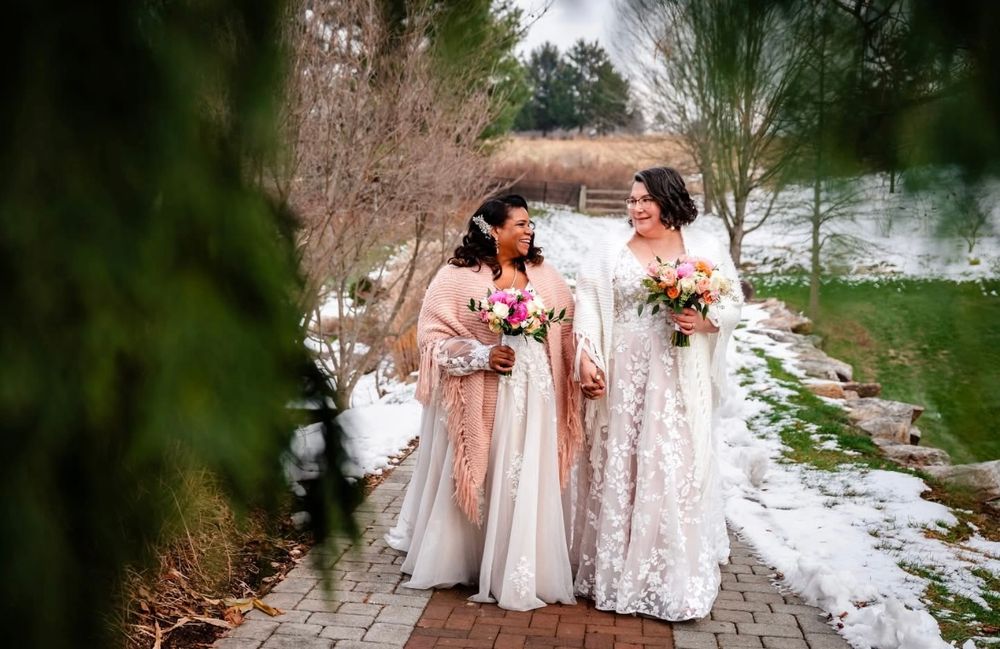 A group of bridesmaids in pink and white dresses gather on a stone path in a garden setting.
