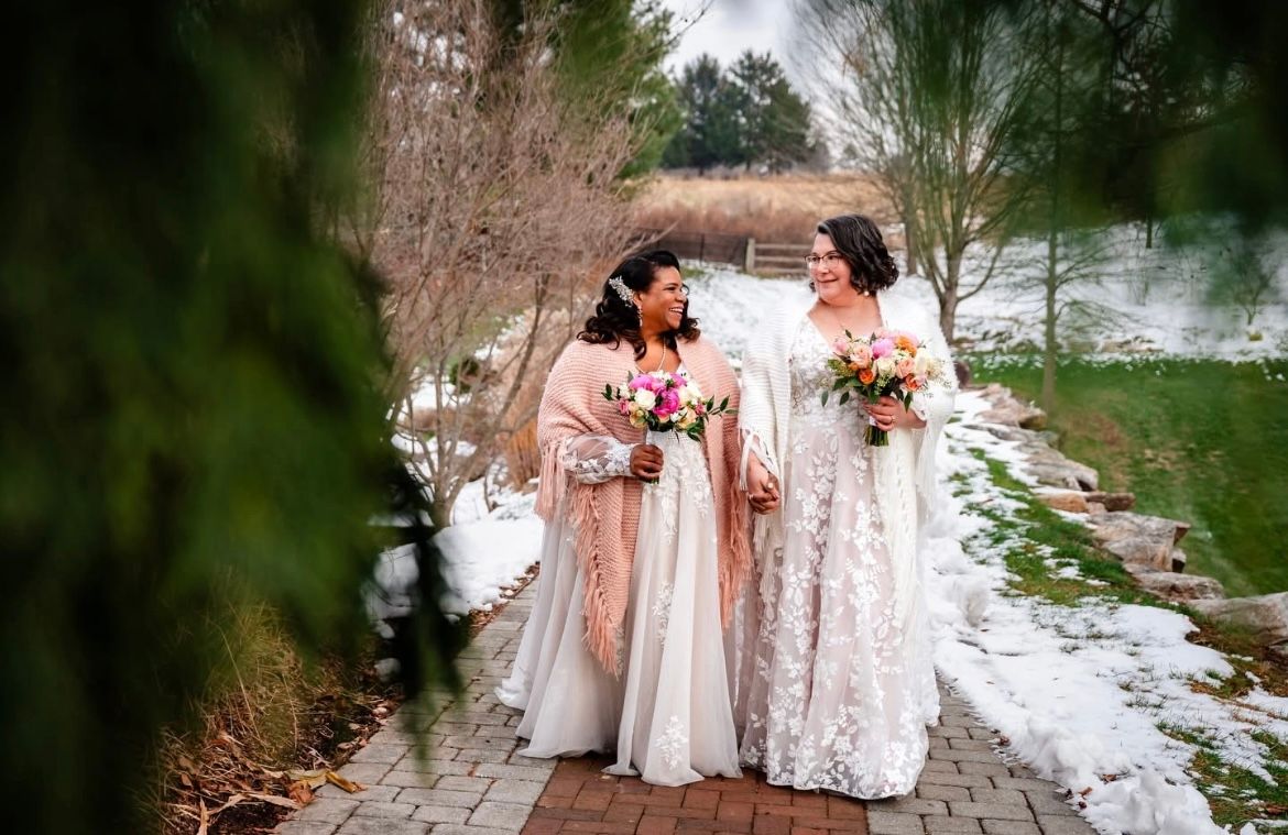 A group of bridesmaids in pink and white dresses gather on a stone path in a garden setting.