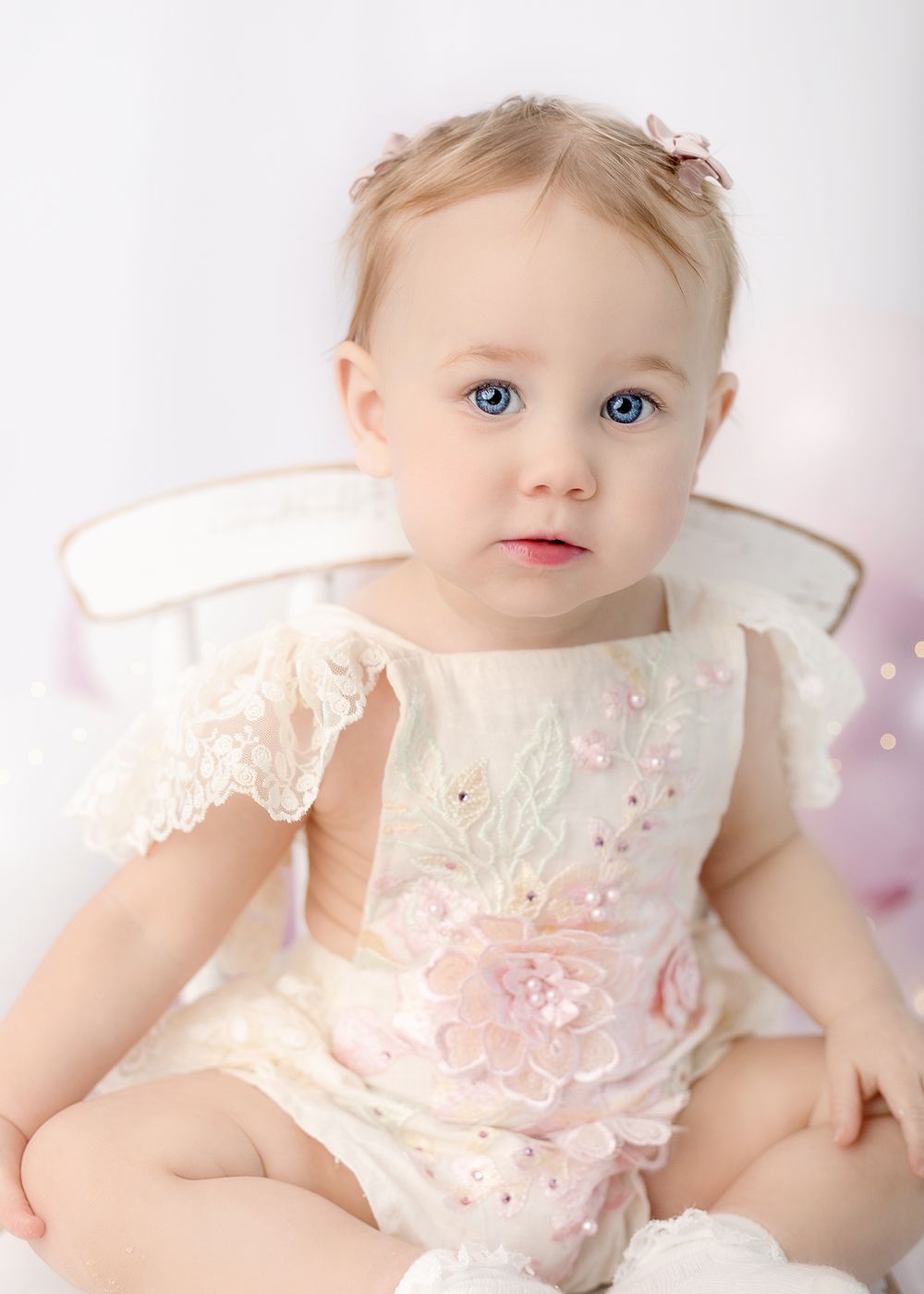 Baby wearing delicate white lace dress with embroidered details.
