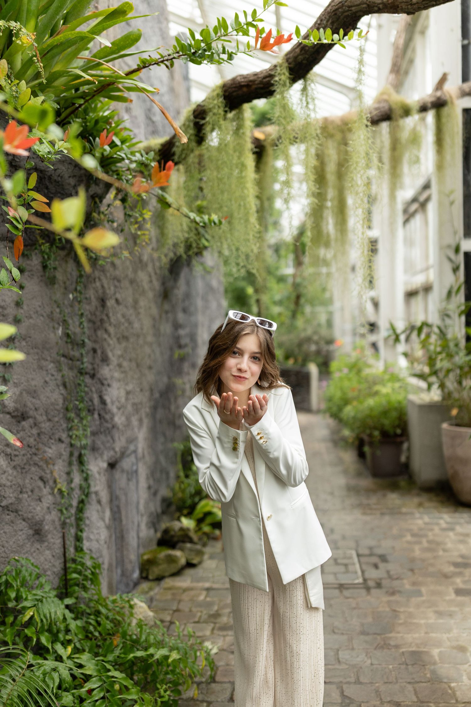 A series of outdoor portraits showing someone in a white jacket and beige dress posing along a stone pathway with greenery.