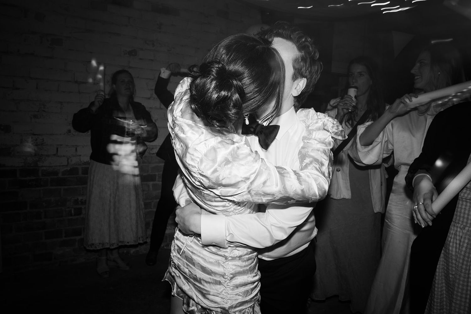 Black and white photo of people dancing and celebrating at a party with string lights overhead.