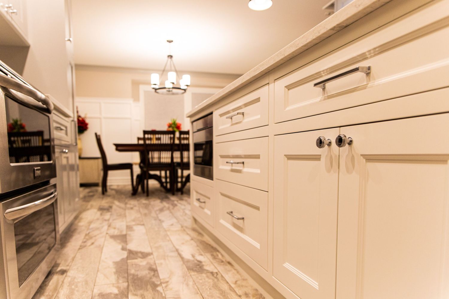 Modern white kitchen interior with marble countertops, white cabinets and stainless steel appliances in luxury home.