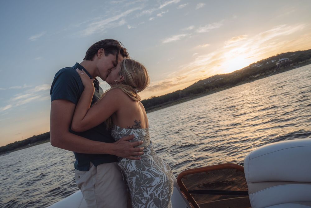 Couple sharing a romantic kiss on a luxury boat at sunset over calm waters.