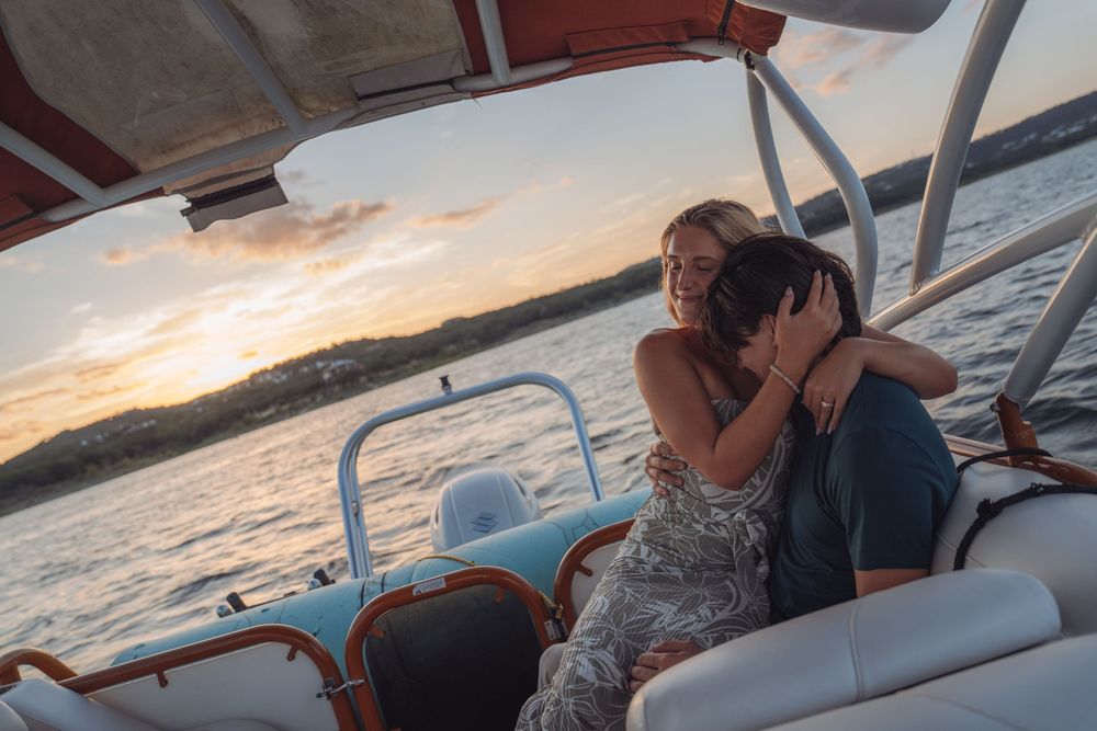 Couple embracing on a boat at sunset, sharing a romantic moment on the water with a colorful sky backdrop.