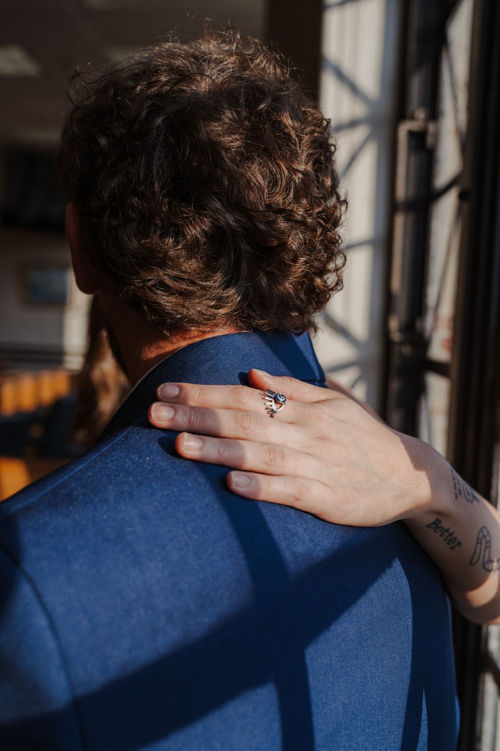 A close-up of a hand with a ring resting on a navy blue suit jacket.