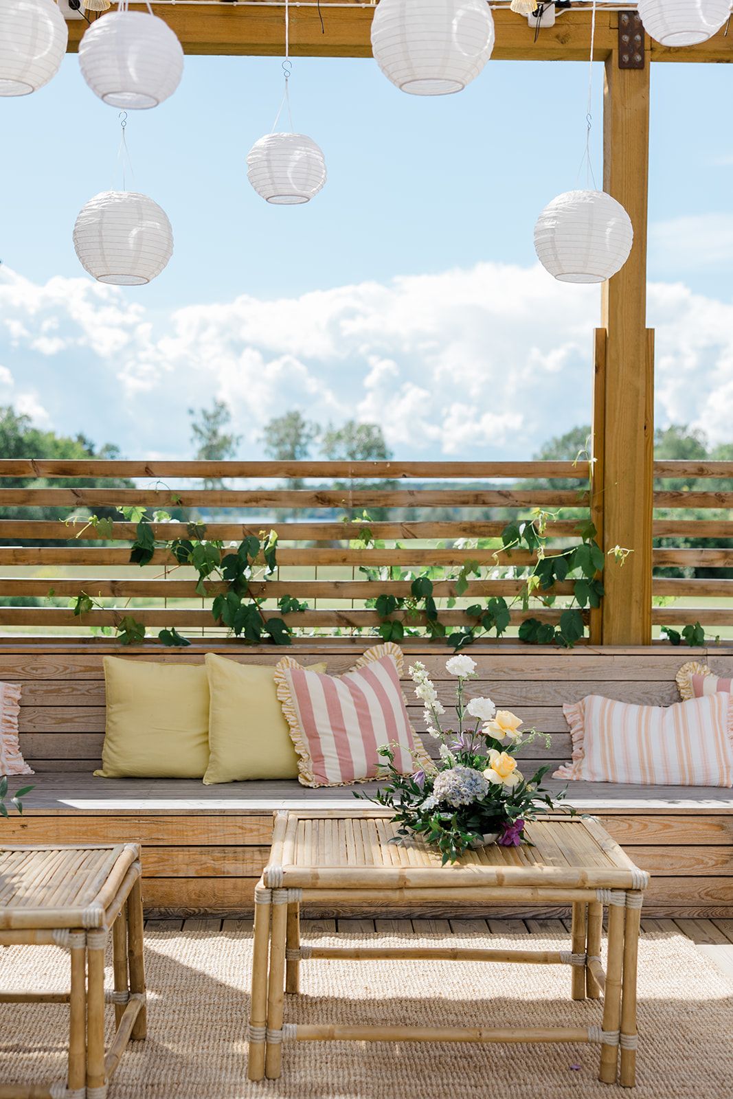 Rustic bamboo lounge seating with cream cushions and floral arrangements on an outdoor deck creates a cozy atmosphere.