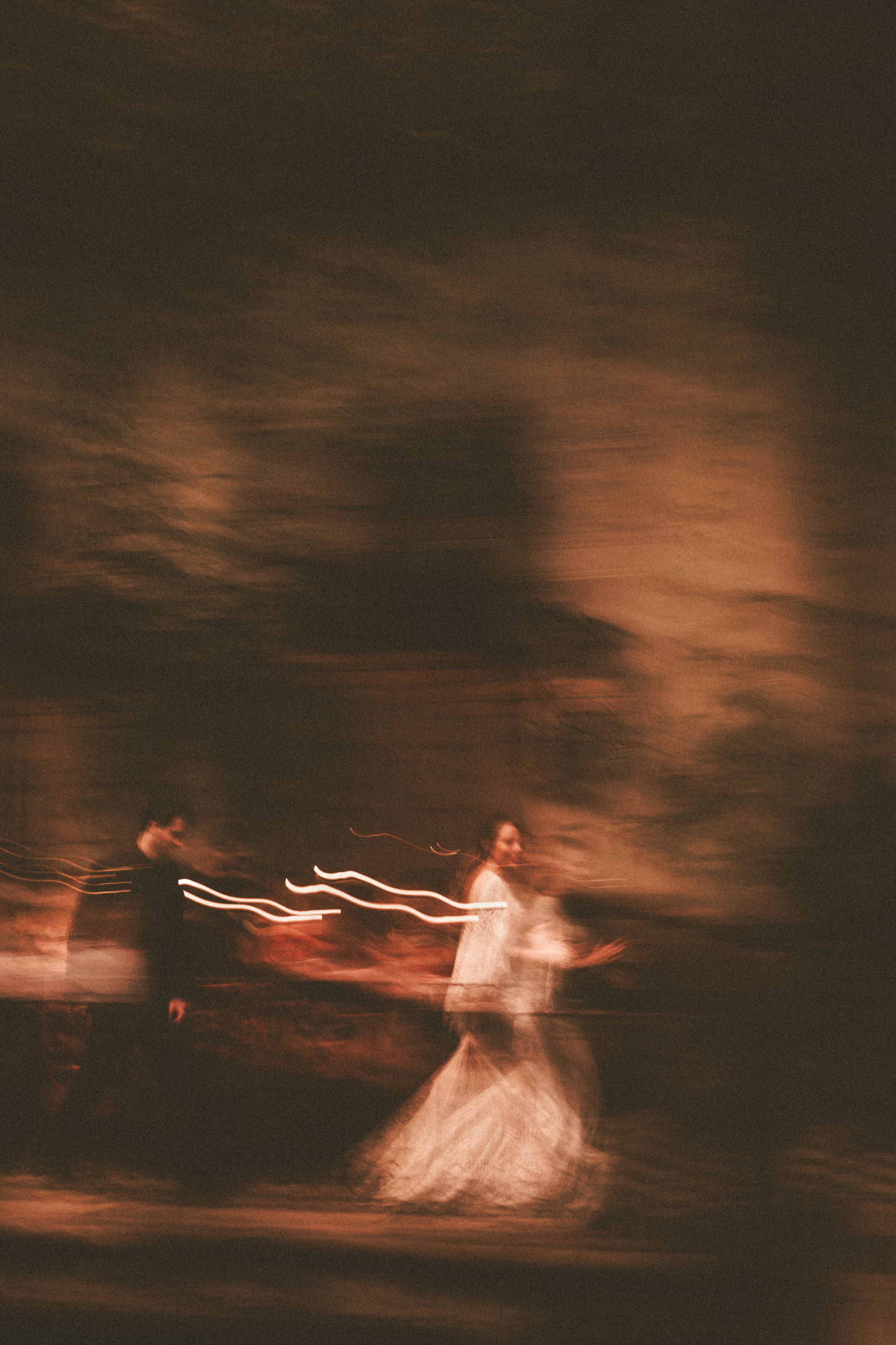 Blurred motion capture of dancers in formal attire creating ethereal light trails against a dark background.