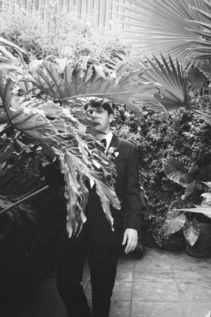 Black and white photo series showing a person in formal attire holding large tropical palm leaves and foliage.