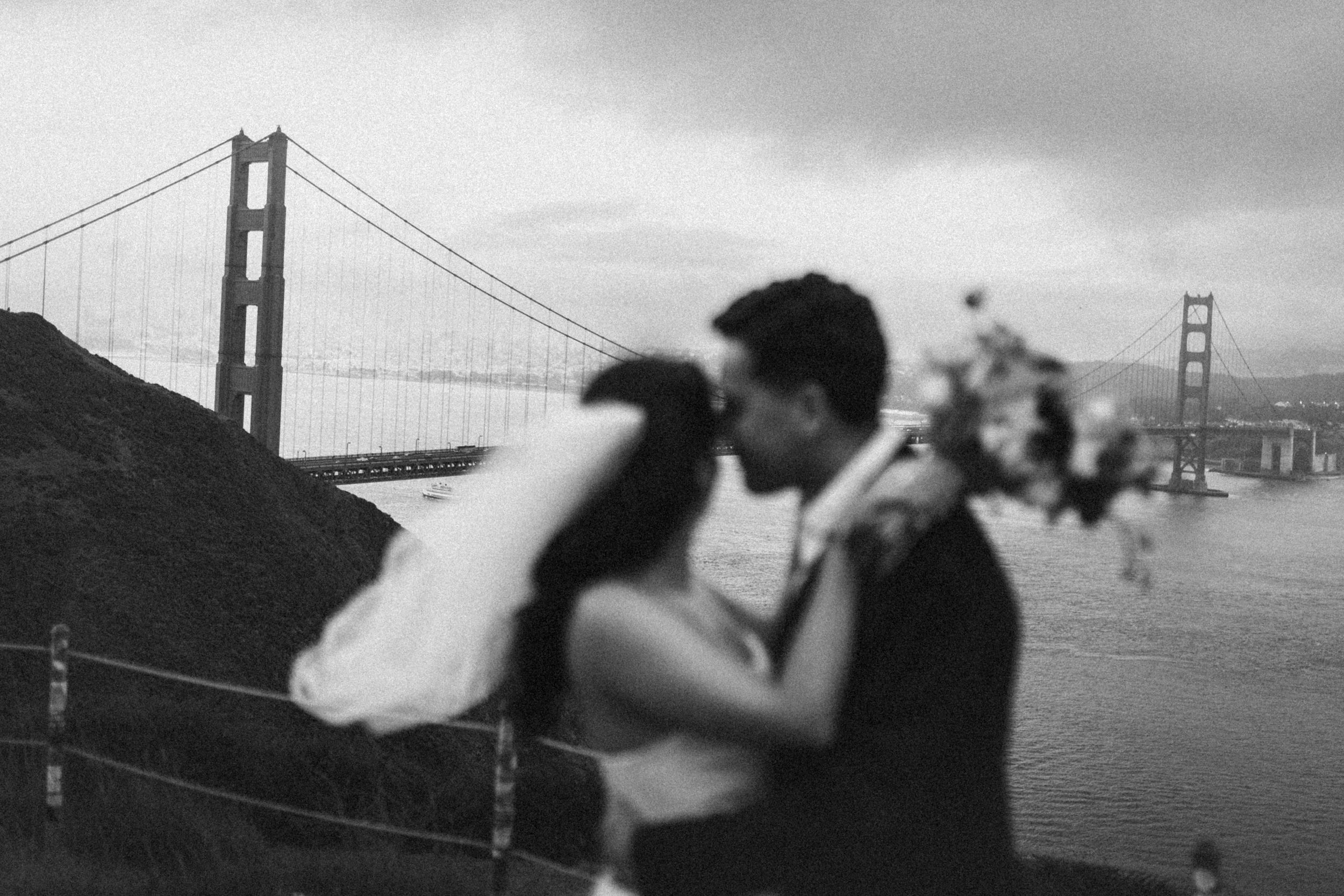 Couple embraces near the Golden Gate Bridge in San Francisco during a cloudy day with moody atmosphere.