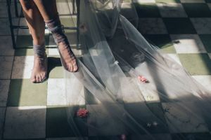 Close-up detail of bride's dress and shoes walking across checkered floor.