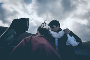 Silhouette of couple against dramatic cloudy sky with car in background.