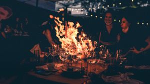Large bonfire illuminating an outdoor dinner table setup at night.