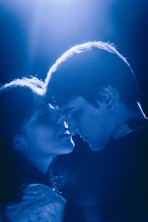 An intimate silhouette of a couple about to kiss in dramatic blue lighting.