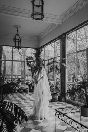 Elegant wedding dress displayed in sunlit conservatory with checkerboard floor and hanging lanterns.