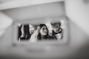 Wedding couple reflected in rearview mirror of vehicle.