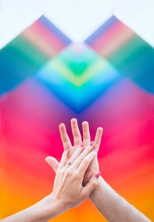 Two hands reach toward each other against a vibrant rainbow geometric background.
