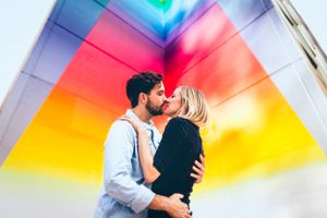 Couple embracing against vibrant rainbow-colored wall backdrop.