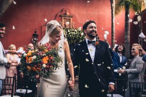 Wedding celebration scene with guests throwing confetti against coral colored wall.