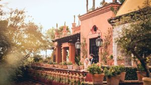 Scenic view of pink Spanish colonial architecture with palm trees and lanterns.