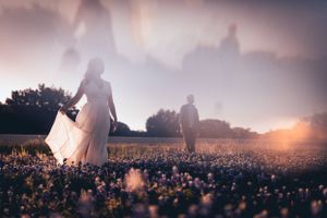 Silhouettes of a couple walking through a dreamy flower field at sunset with ethereal light and blooms.
