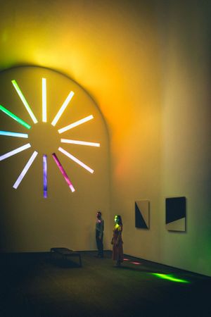Art installation featuring neon light rays against minimalist yellow wall.