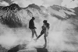 A black and white photo of playful movements in front of snow-capped mountains.