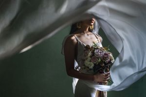 Artistic wedding photograph with flowing veil and bouquet against soft background.
